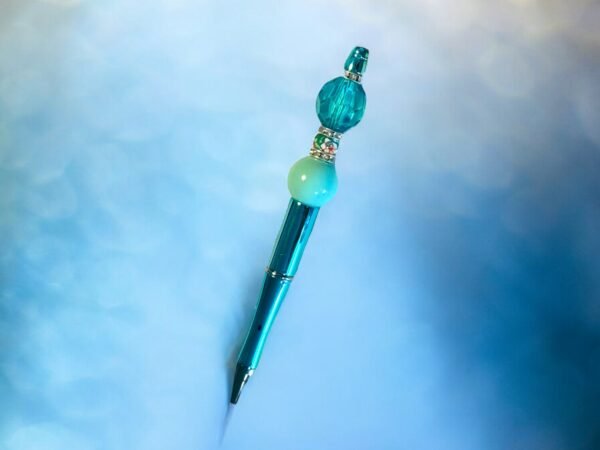A shimmering teal pen with decorative turquoise and mint green beads on a blue surface.
