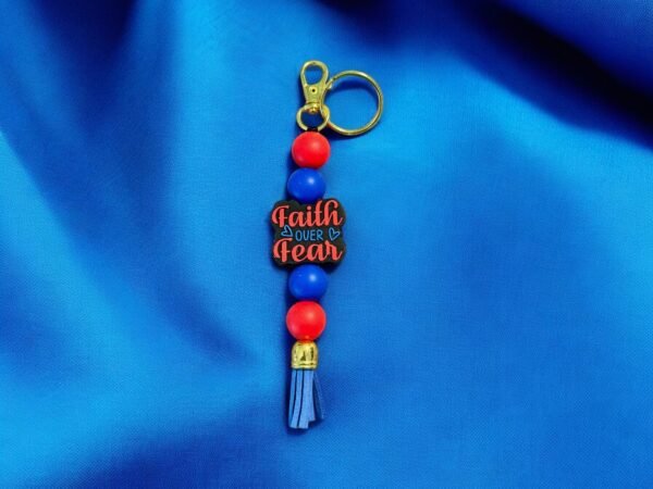 A keychain with alternating red and blue beads, a blue tassel, and a charm reading "Faith over Fear."