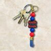 A keychain with keys, red and blue beads, and a charm that says Faith Over Fear on a marble surface.
