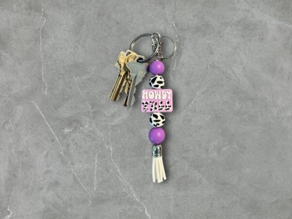 Keychain with metal keys, purple and cow print beads, and a pink "HOWDY Y'ALL" charm.
