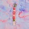 A pink beaded keychain with a butterfly bead, light pink tassel, and gold clasp on a marbled surface.