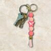 A cluster of keys connected to a vibrant pink beaded keychain with a butterfly charm and tassel.