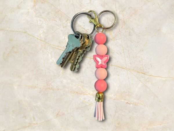 A cluster of keys connected to a vibrant pink beaded keychain with a butterfly charm and tassel.