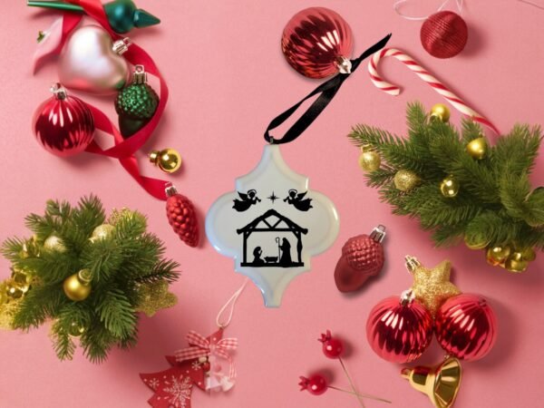 A white ornament featuring a black Nativity scene with angels, surrounded by colorful Christmas decor.