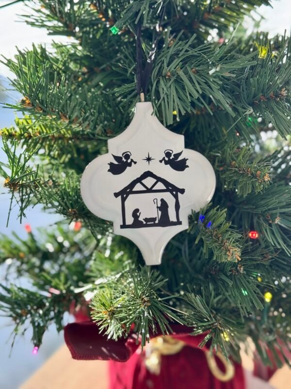 White ornament featuring a black Nativity scene of Mary, Joseph, baby Jesus, angels, and a star