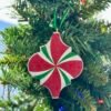 A shimmering red, green, and white swirled Christmas ornament hangs on a green tree.