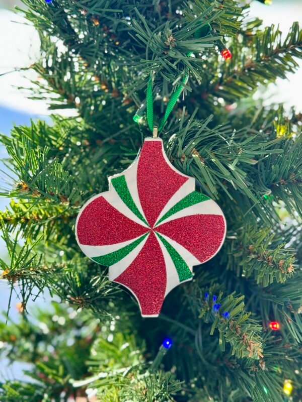 A shimmering red, green, and white swirled Christmas ornament hangs on a green tree.
