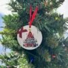 Round white Christmas ornament with a red plaid tree, gifts, and 'merry christmas' text.