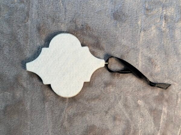 A white quadrilobed felt ornament with a black ribbon loop on a gray fuzzy surface.