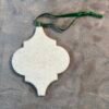 White felt ornament with an arabesque shape and a green ribbon on a gray fuzzy surface.