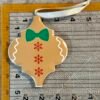 A tan gingerbread man ornament, with a green bow tie and red snowflakes, on a measuring ruler.