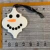 A white snowman-shaped ornament featuring black eyes, an orange glitter nose, and a black ribbon.