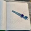 A decorative silver pen with purple and turquoise beads rests on an open lined notebook.