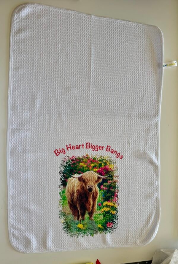 White waffle-weave towel with a shaggy brown Highland cow, colorful flowers