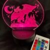 A glowing pink acrylic lamp features an etched design of a dragon, castle, open book, crescent moon