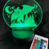 Illuminated green LED lamp displaying a dragon, castle, moon, and stars design, next to a remote control.