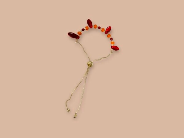 A bracelet with an arc of red and orange beads on a golden adjustable chain.