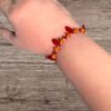 An arm wears an orange and red beaded bracelet with red teardrop beads and a gold chain on wood.