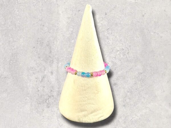 A colorful beaded bracelet with pink, blue, and gold beads rests on a cream display cone.