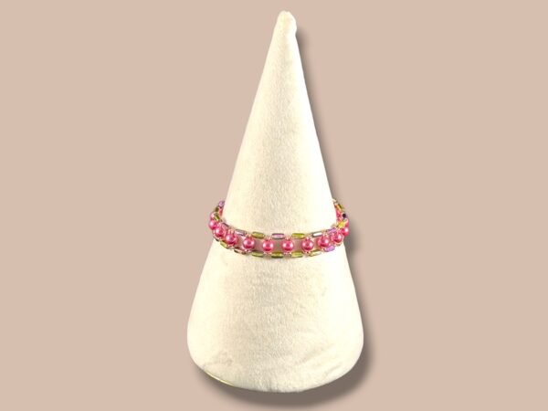 A pink and green beaded bracelet with spherical and rectangular beads on a cream cone stand.