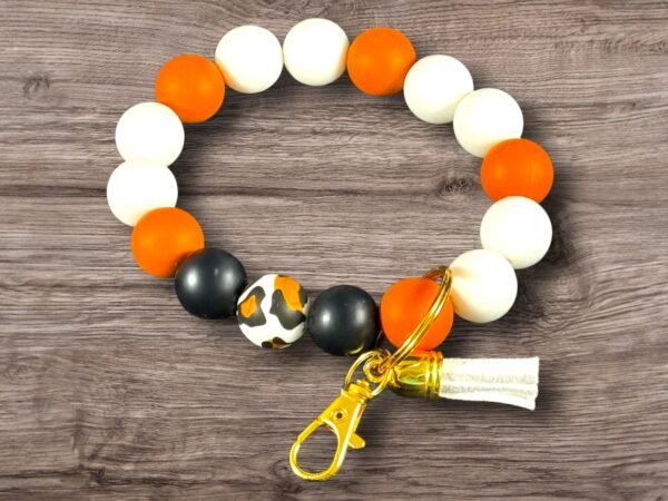 Round silicone beaded keychain with white, orange, black, leopard print beads, gold clasp, and white tassel.