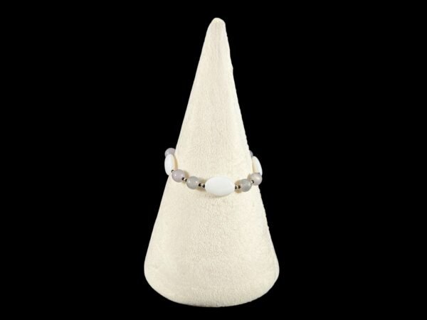 Close-up of a white and gray beaded bracelet elegantly displayed on a velvety cream cone.