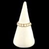 A gold and white beaded ring with small green accents, displayed on a cream velvet cone.