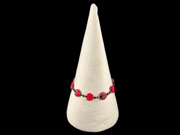 A red beaded bracelet with carved leaf-shaped beads on a white cone display stand.