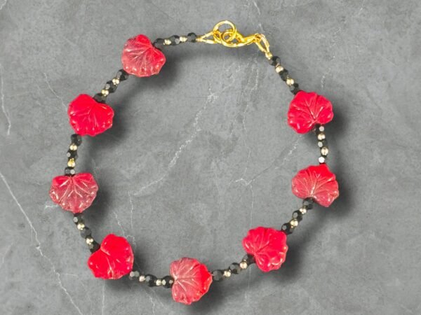 Black beaded bracelet featuring red carved leaf-shaped beads spaced evenly around the strand, accented with small gold and black spacer beads and finished with a gold lobster clasp, displayed on a gray stone background.